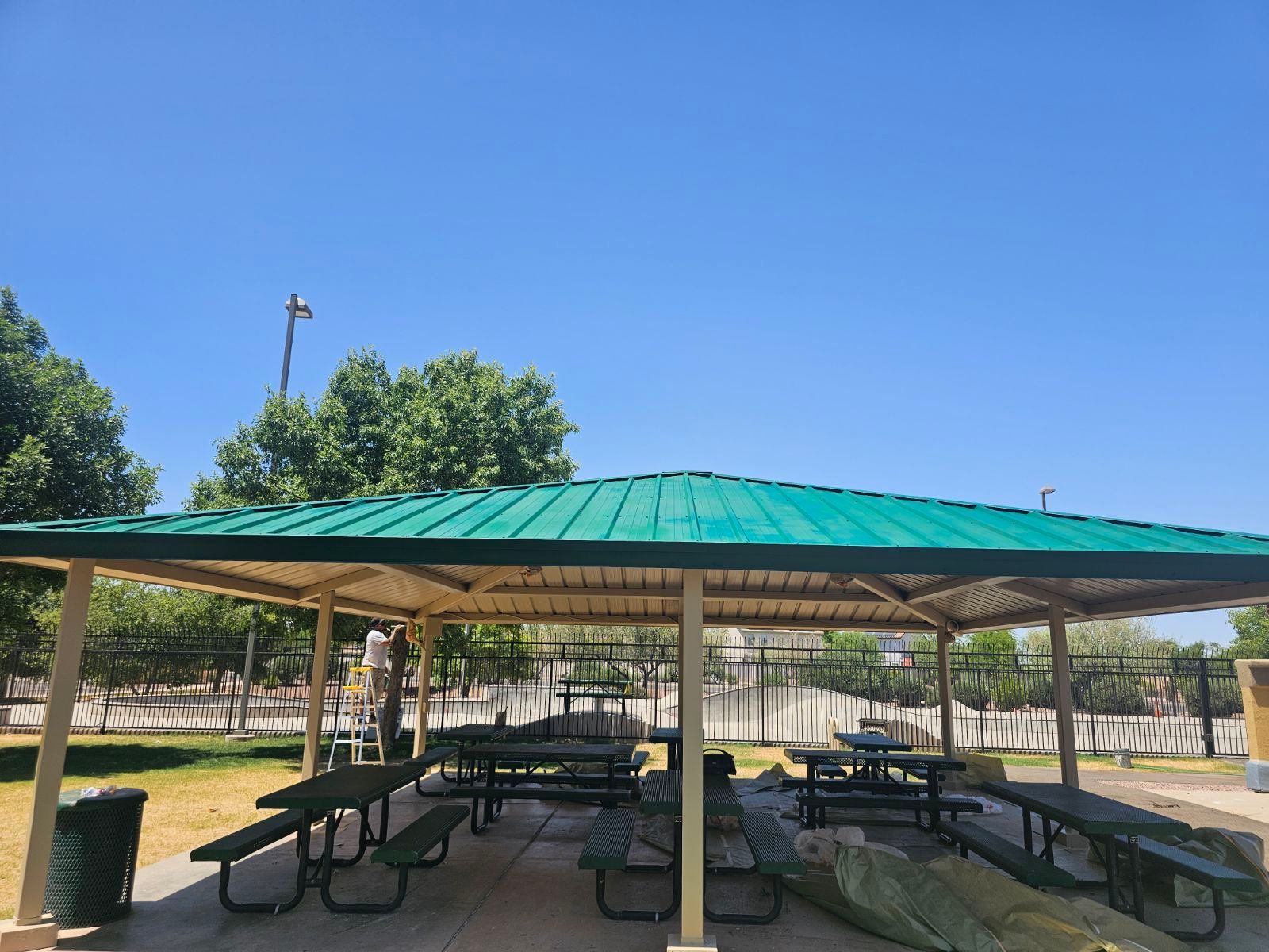 A picnic shelter with tables and benches under a green roof.