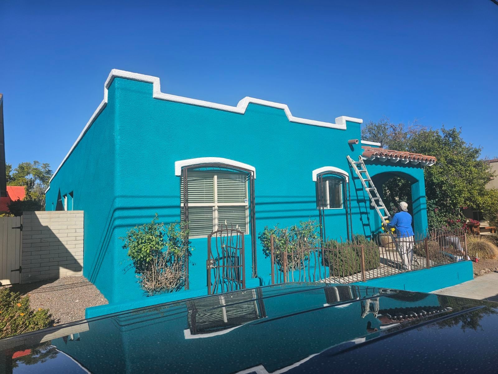 A man is painting a blue house with a ladder.