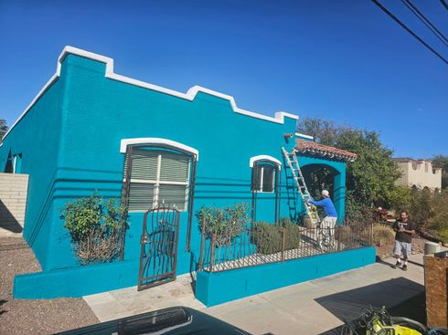 A man is painting a blue house with a ladder