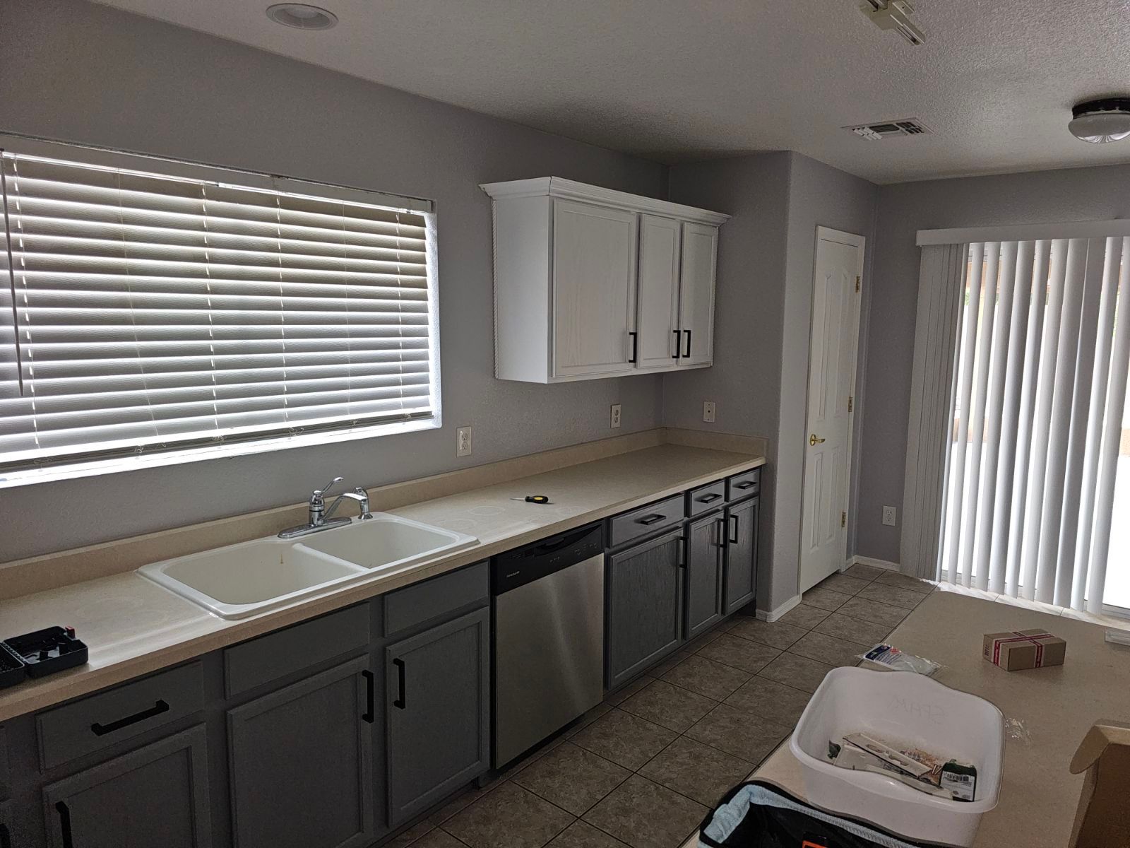 A kitchen with gray cabinets , stainless steel appliances , a sink and a window.