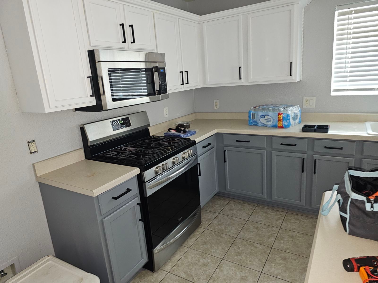 A kitchen with gray cabinets , a stove , microwave , and sink.