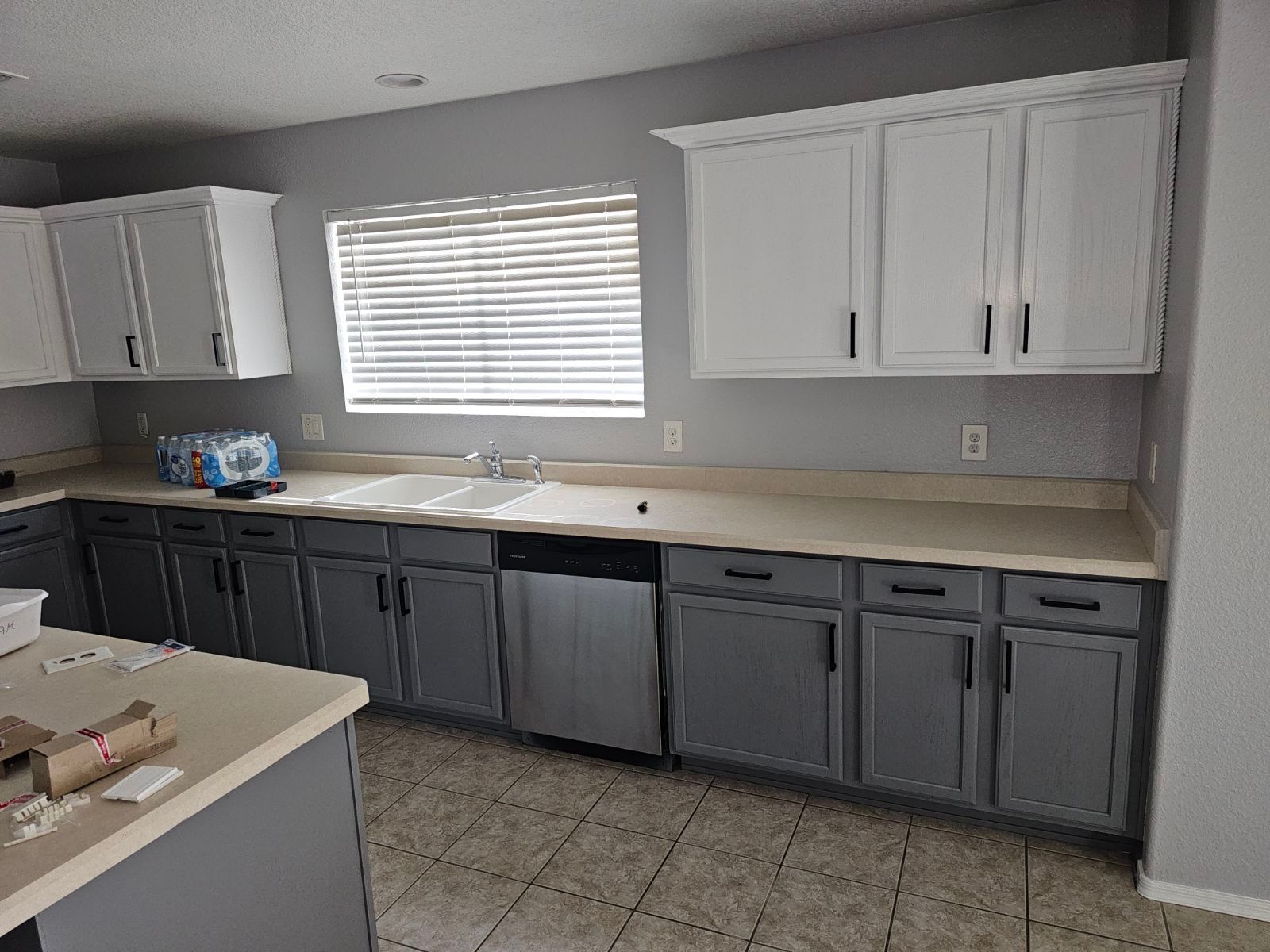 A kitchen with gray cabinets , white cabinets , a sink , and a window.