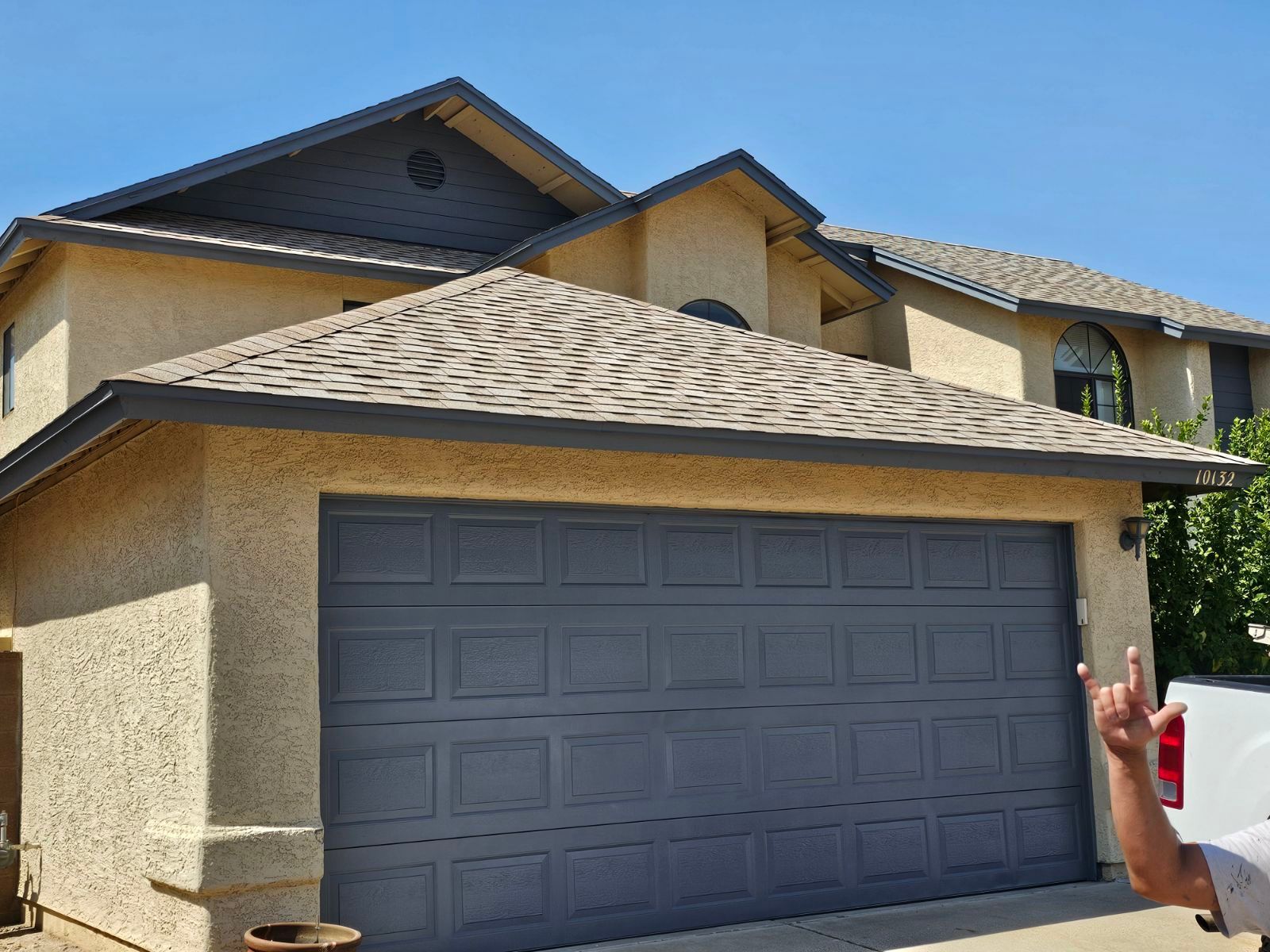 A man is standing in front of a large house with a garage door.
