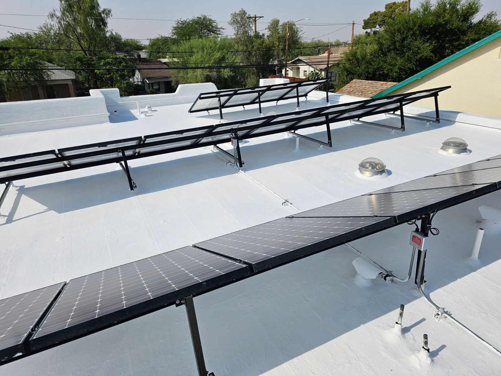 A row of solar panels are sitting on top of a white roof.