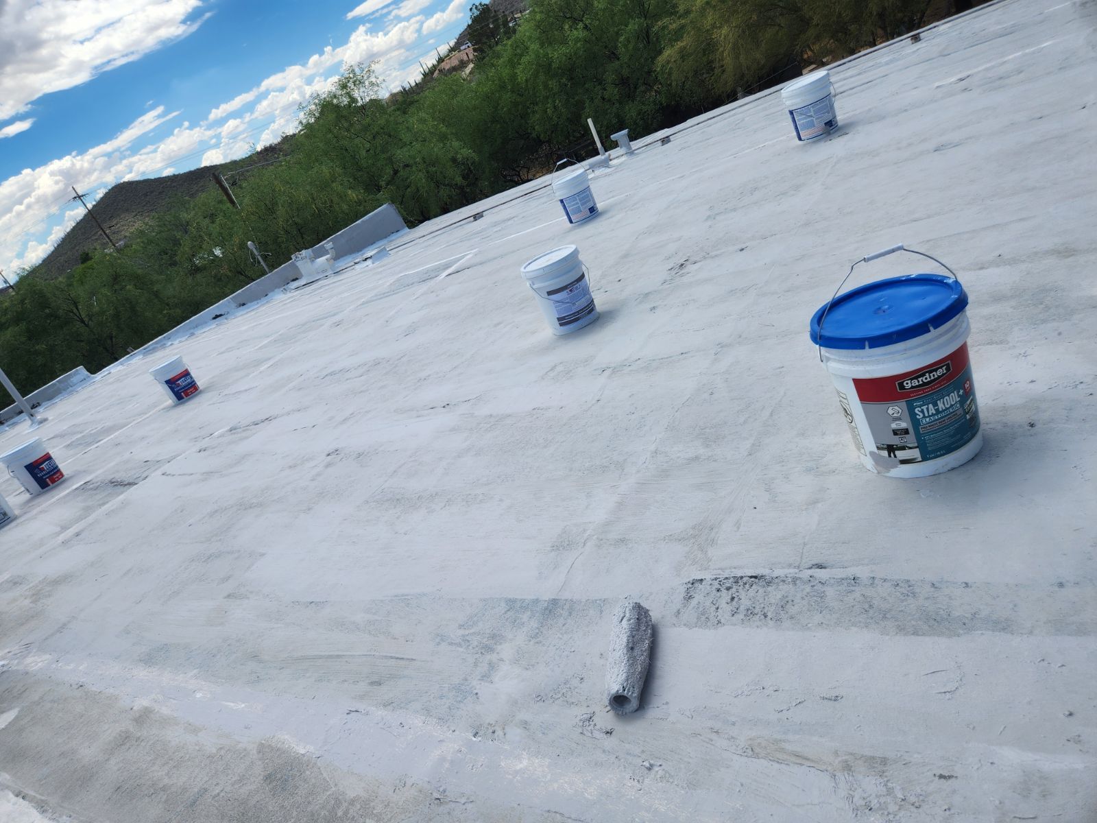 A bucket of paint is sitting on top of a white roof.