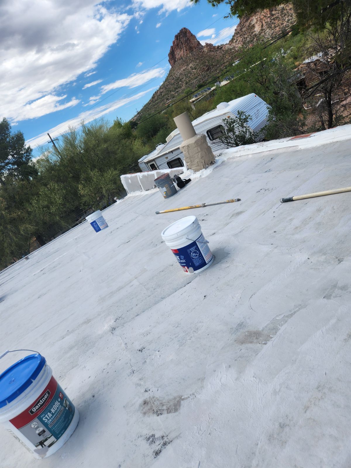 A bucket of paint is sitting on top of a white roof.