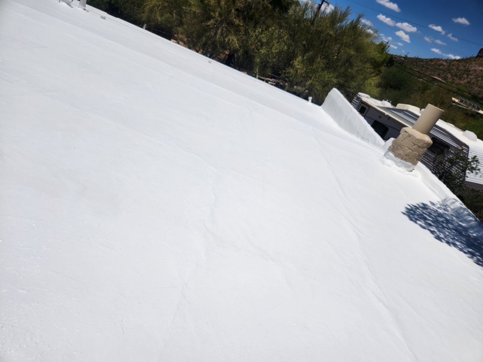 A white roof with a chimney on it and trees in the background.