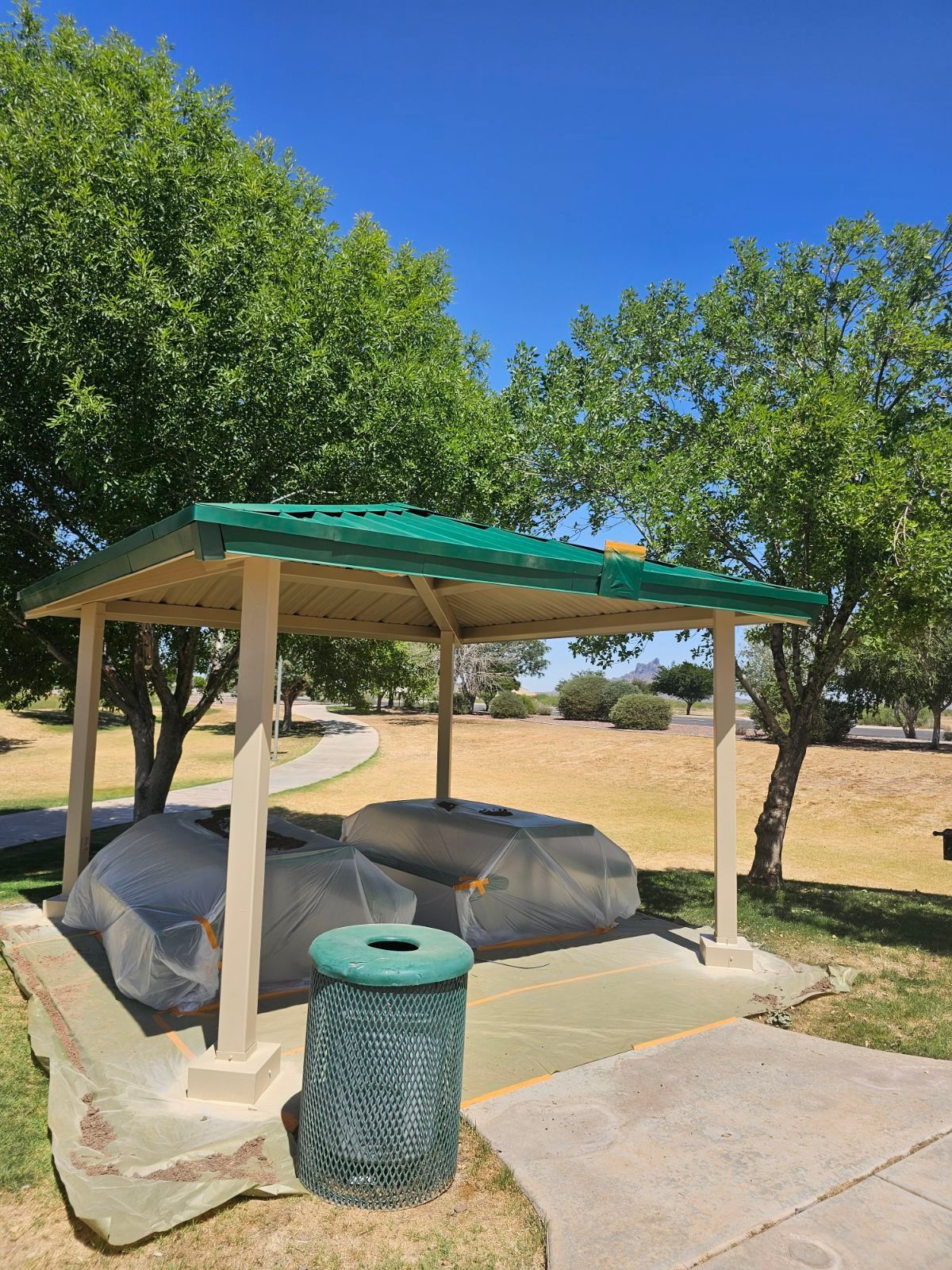 A green trash can is next to a shelter in a park.