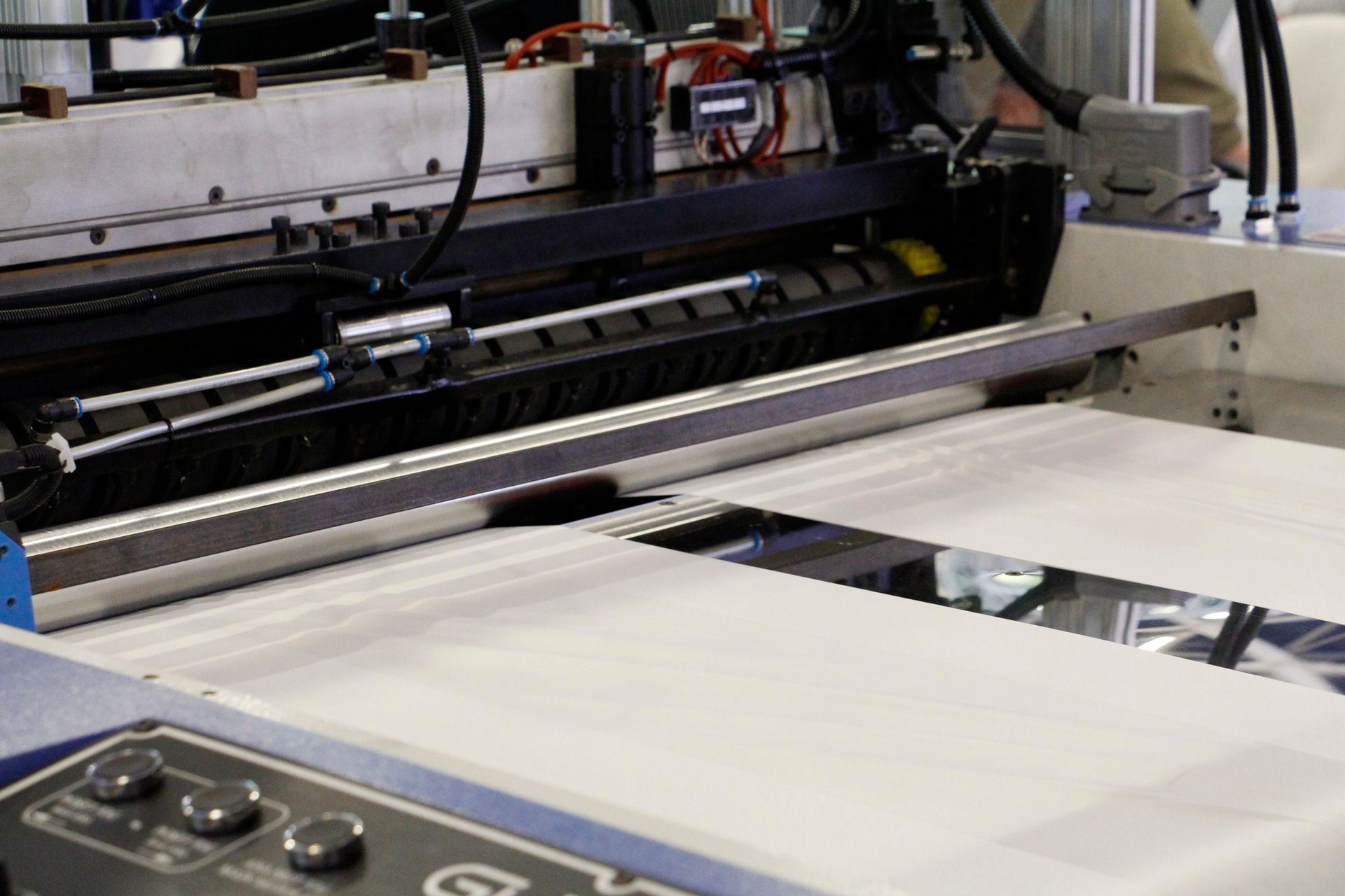 Máquina industrial con una lámina blanca de material pasando por sus rodillos y componentes metálicos.