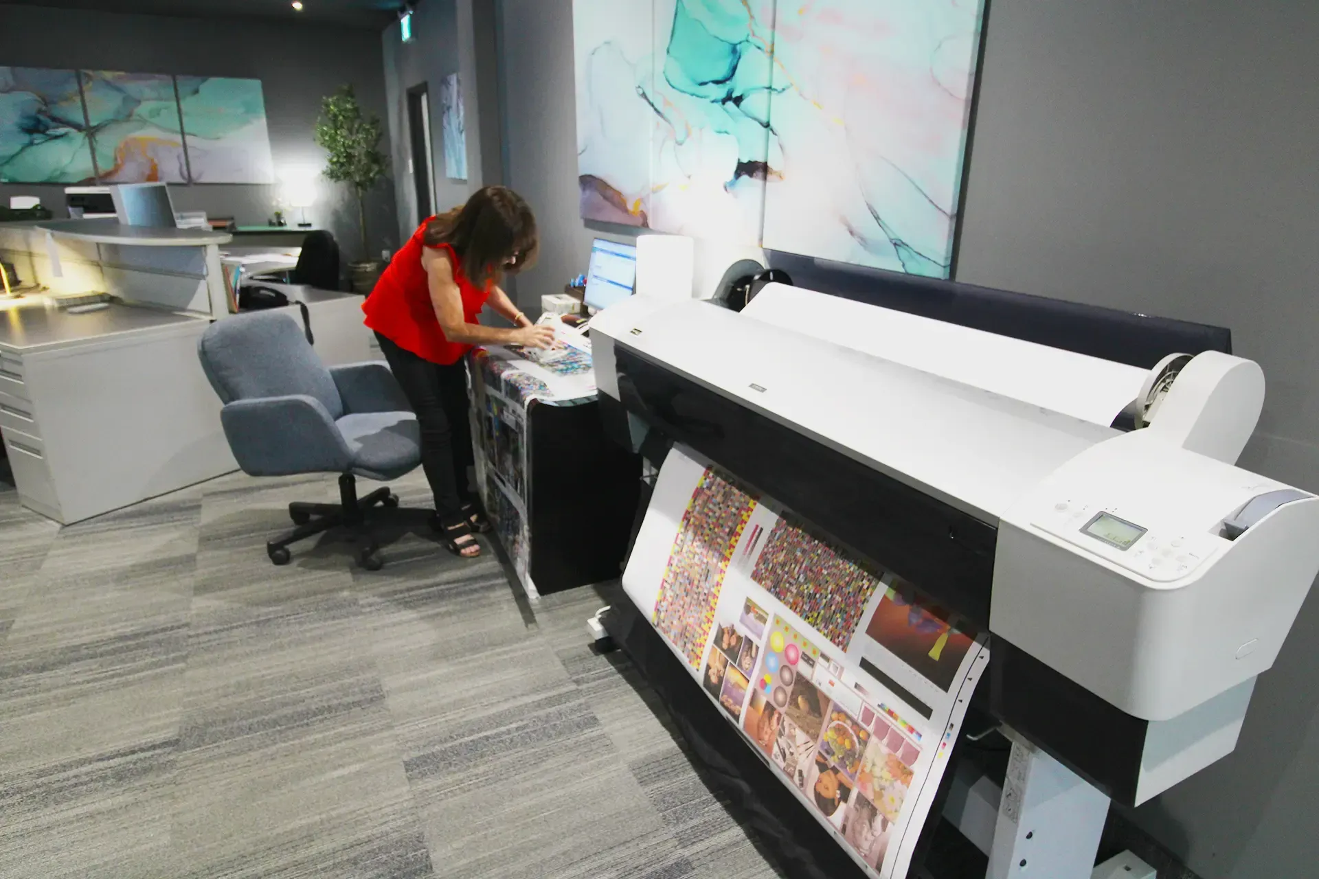 A woman is standing in front of a large printer in an office.