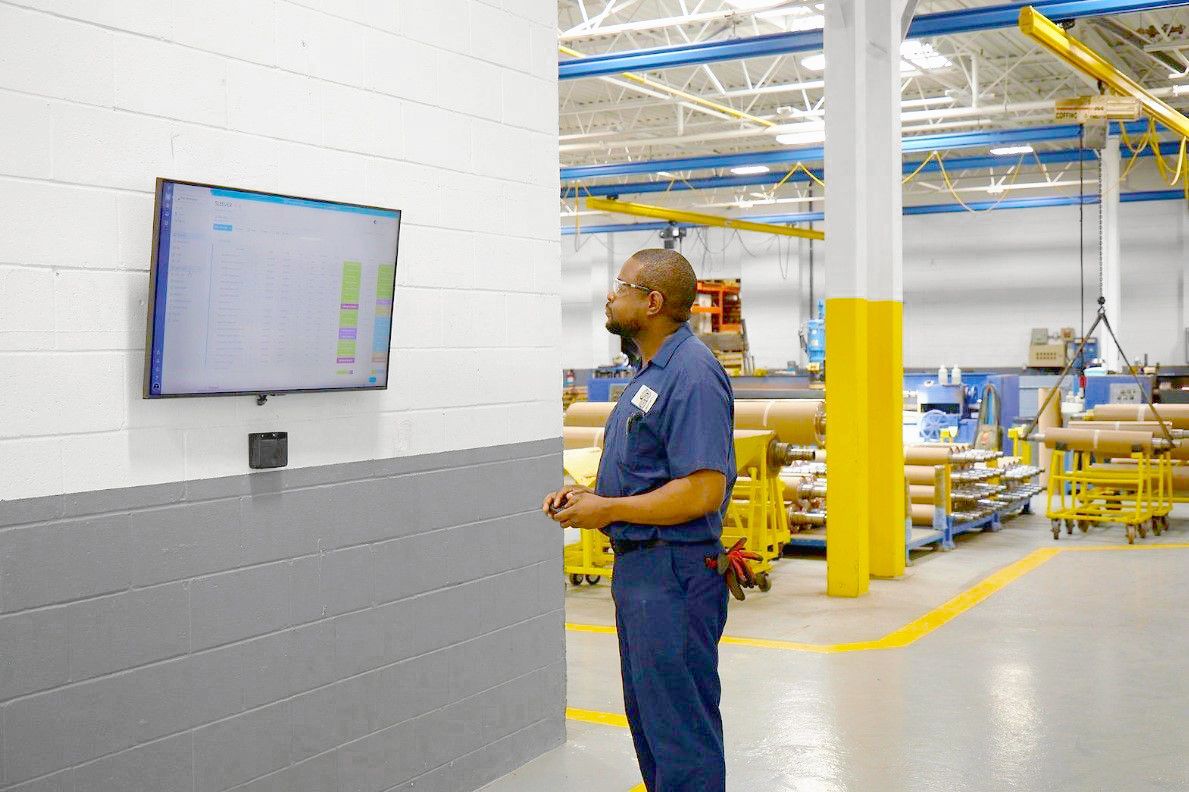 A man is standing in a factory looking at a television.