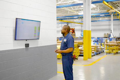 A man is standing in a factory looking at a television.