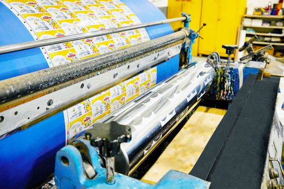 A machine is printing stickers on a sheet of paper in a factory.