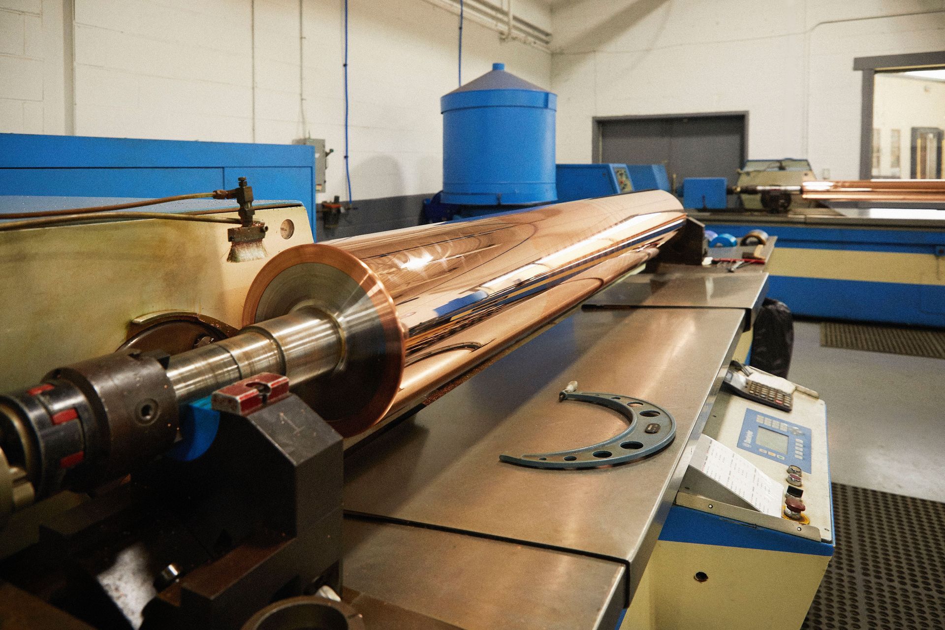 A large copper roller is sitting on top of a machine in a factory.