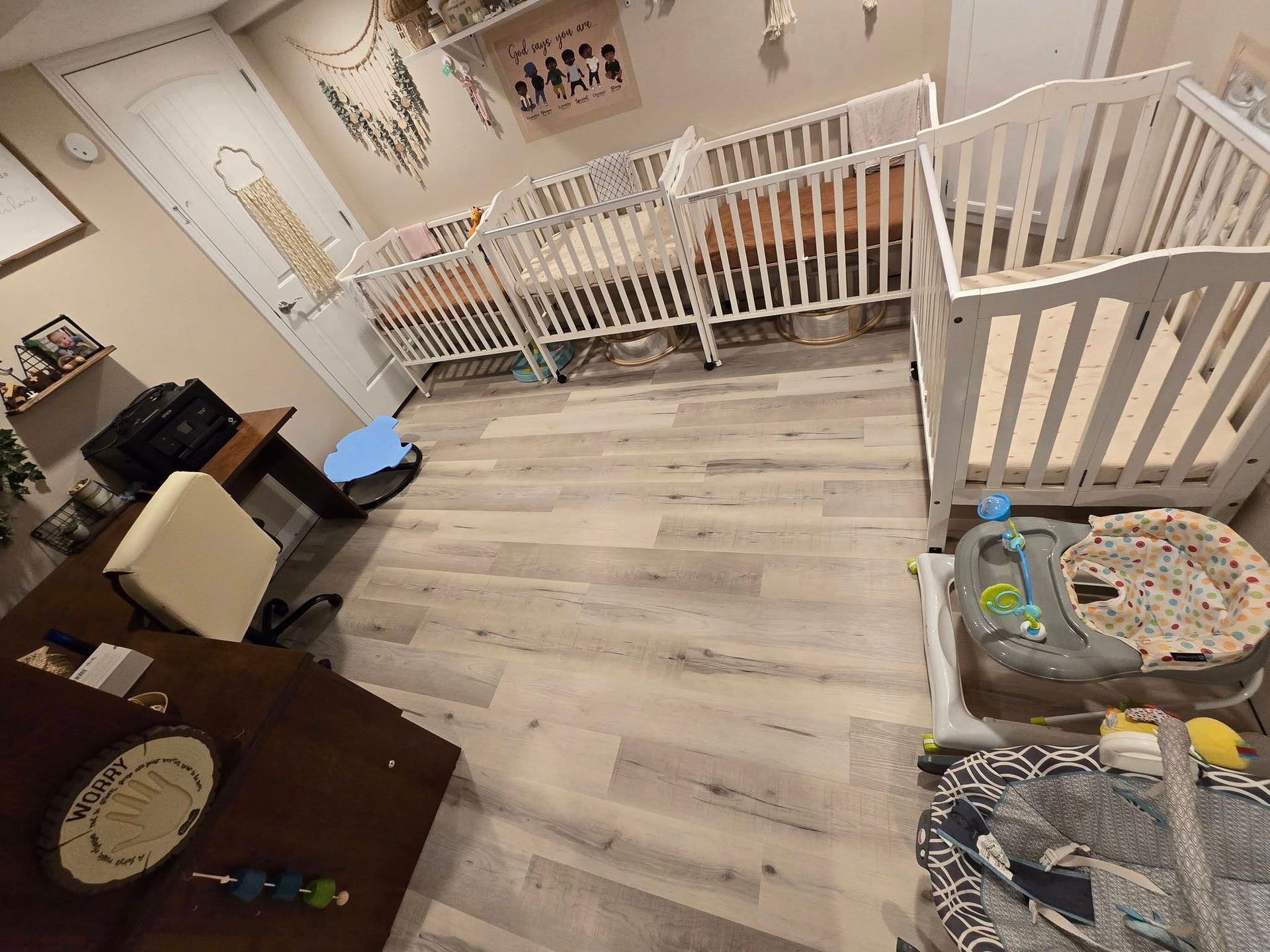 A room with three cribs , a desk , and a chair.