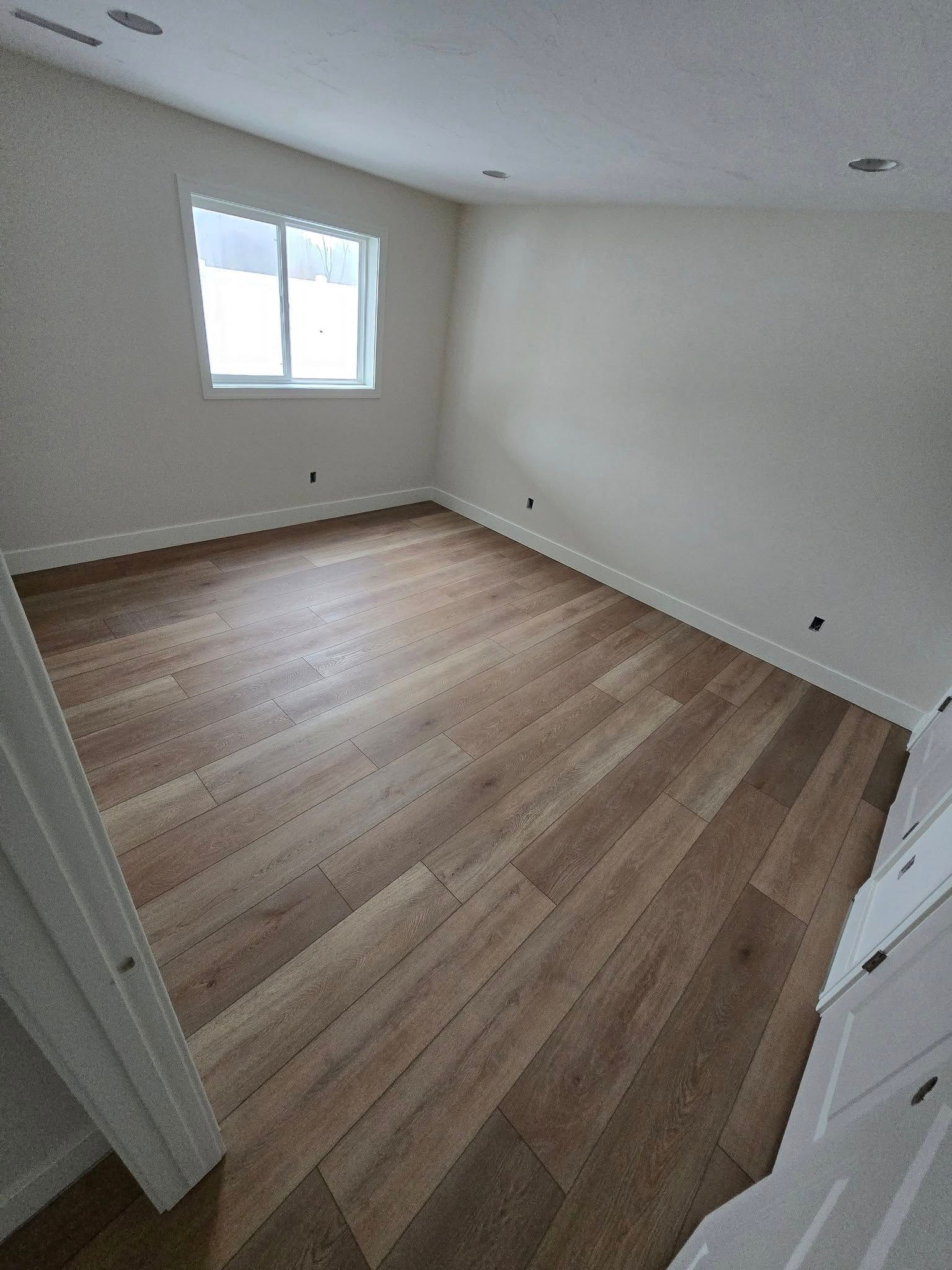 An empty room with hardwood floors and a window.