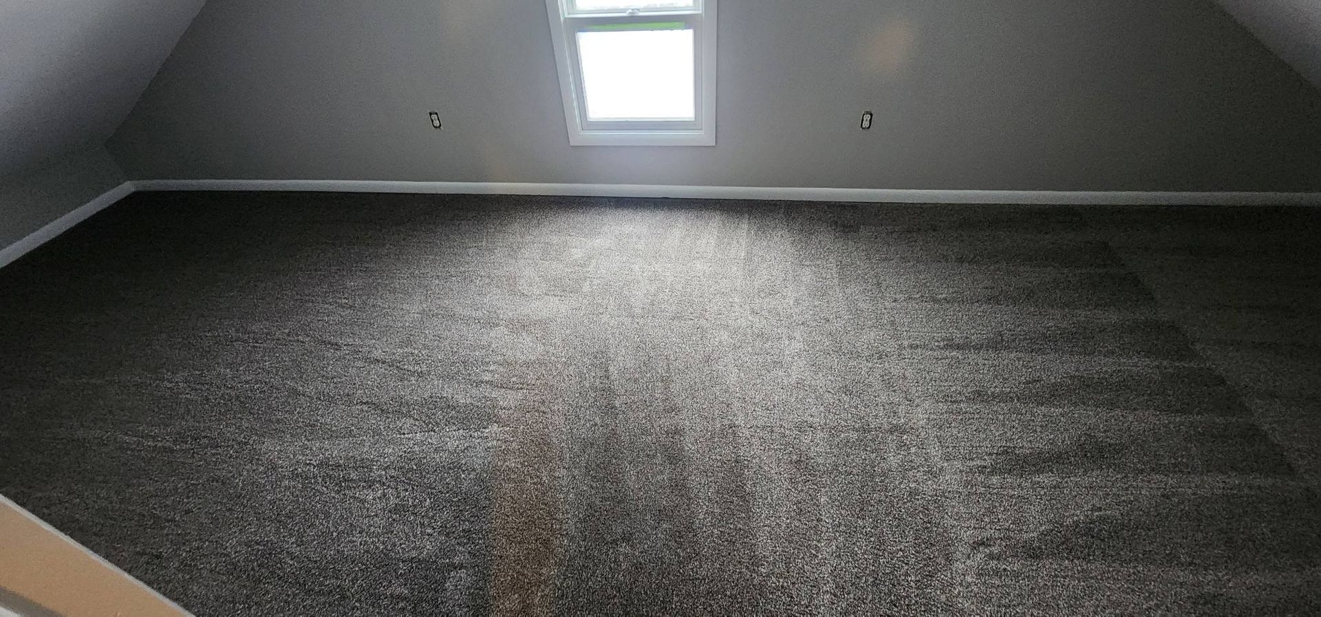 An empty room with a gray carpet and a window.