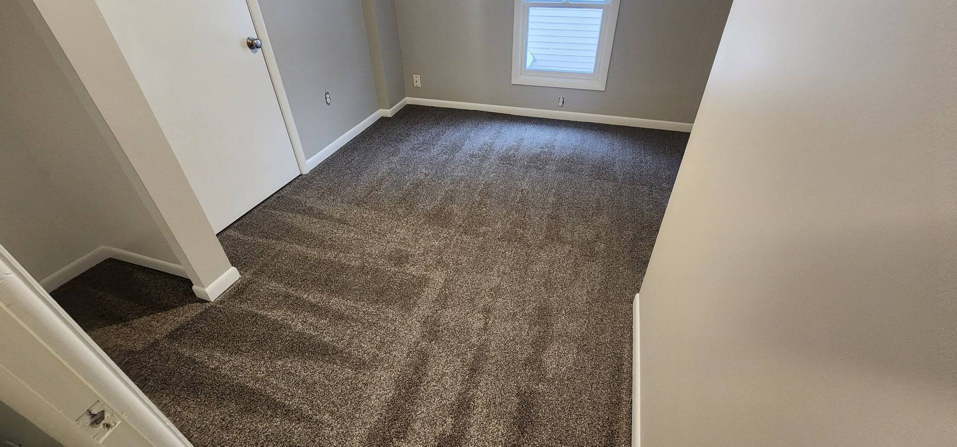An empty room with a carpeted floor and a window.