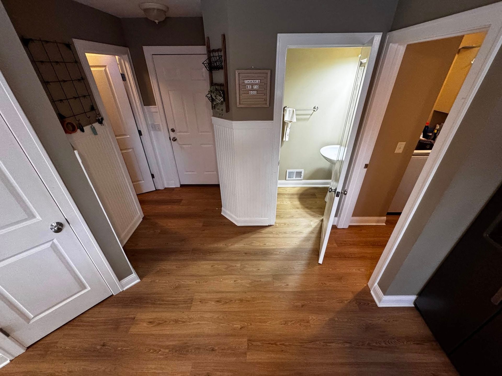 A hallway with hardwood floors and white doors leading to a bathroom.