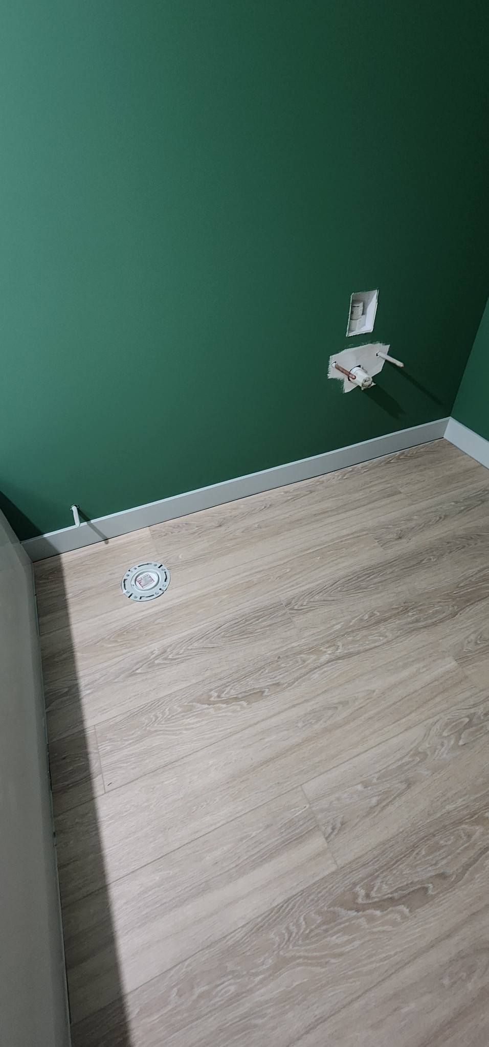 A wooden floor is being installed in a room with a green wall.