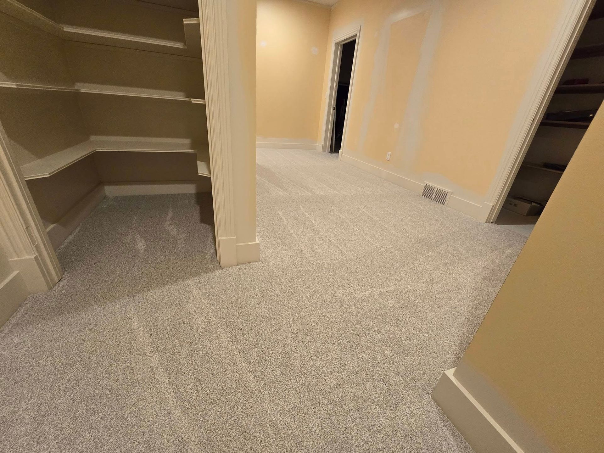 A hallway with carpeted floors and shelves in a house