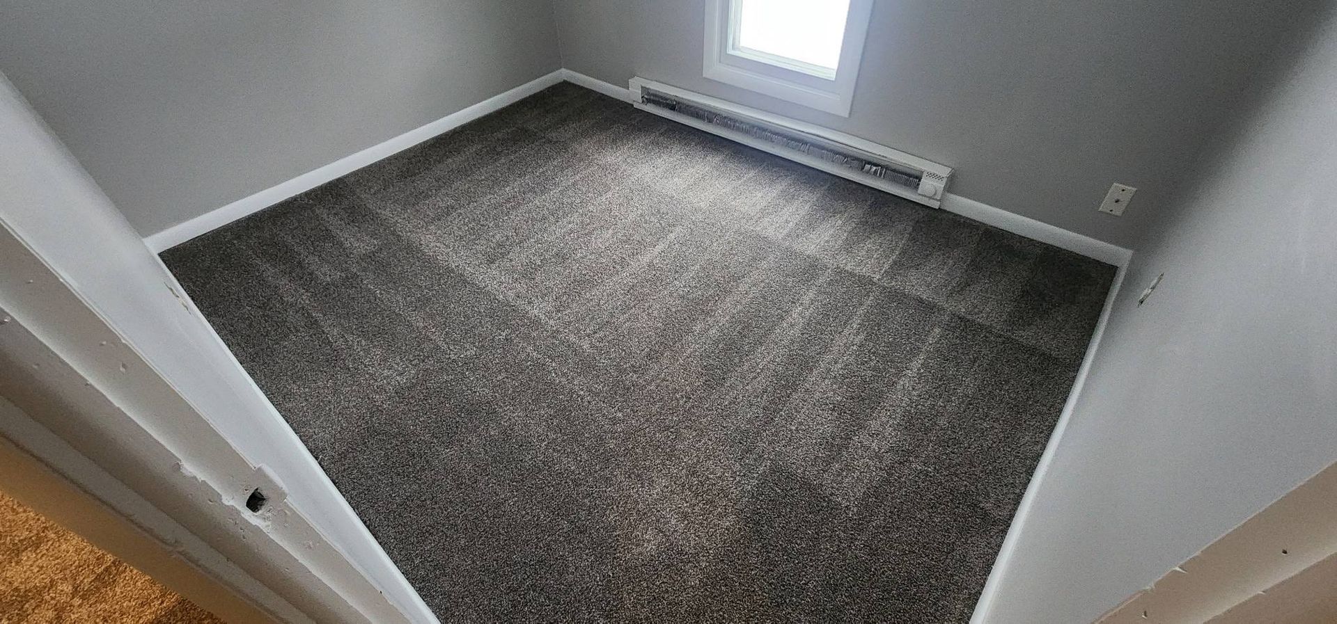 An empty room with a carpeted floor and a window.
