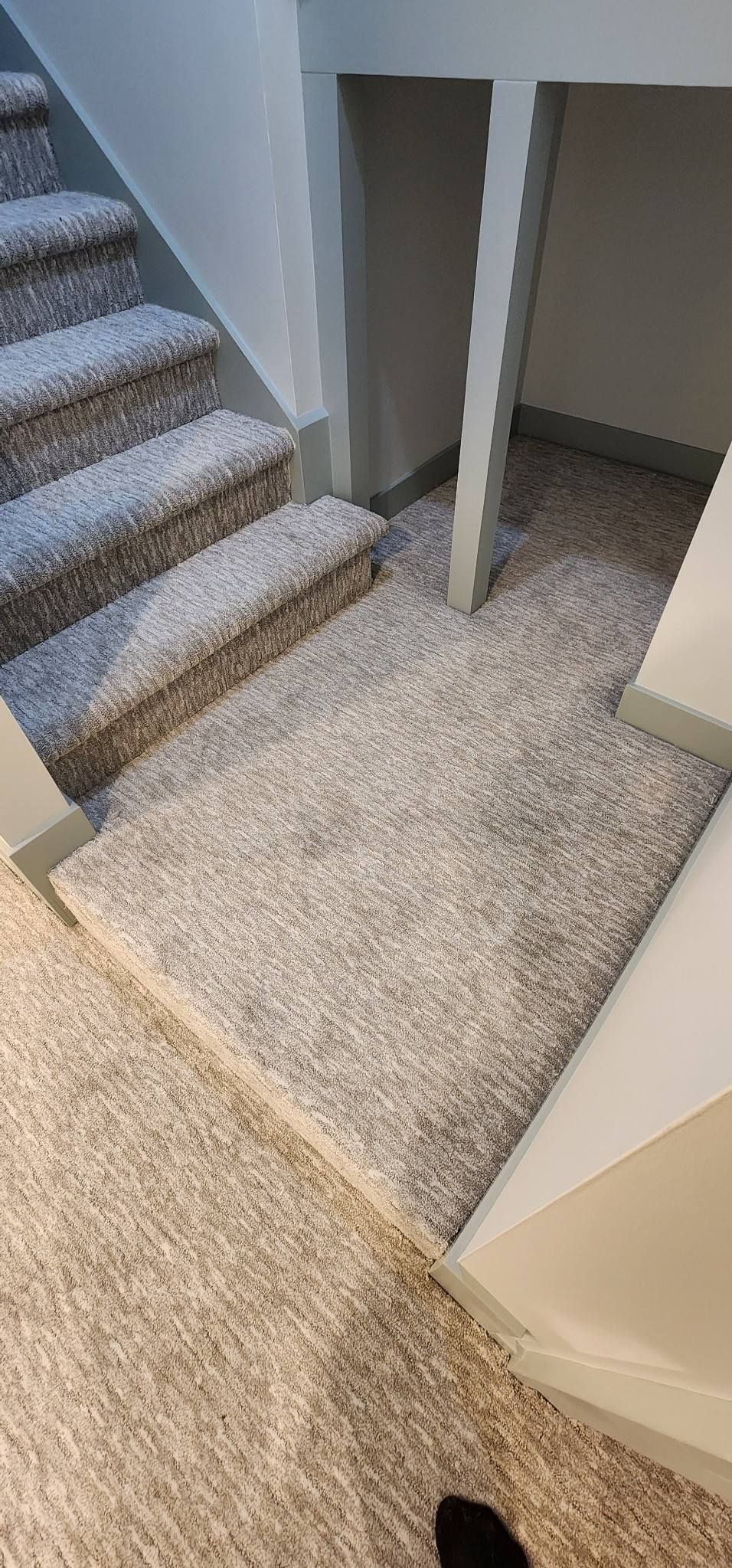A person is standing on a carpeted floor next to a set of stairs.