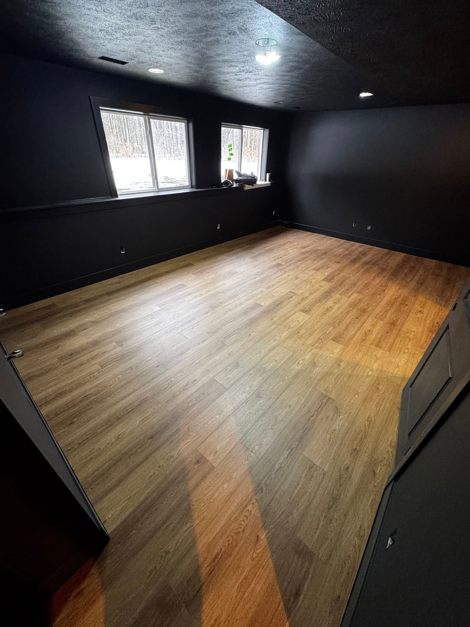 An empty room with a wooden floor and black walls.