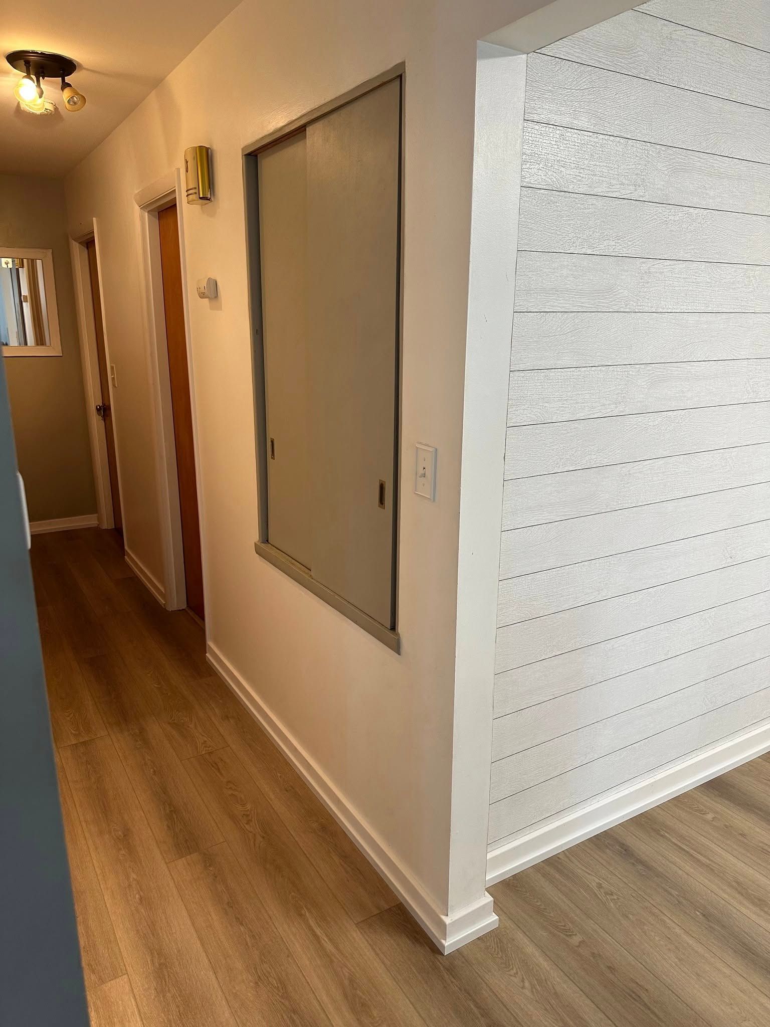 A hallway with hardwood floors , white walls and a window.