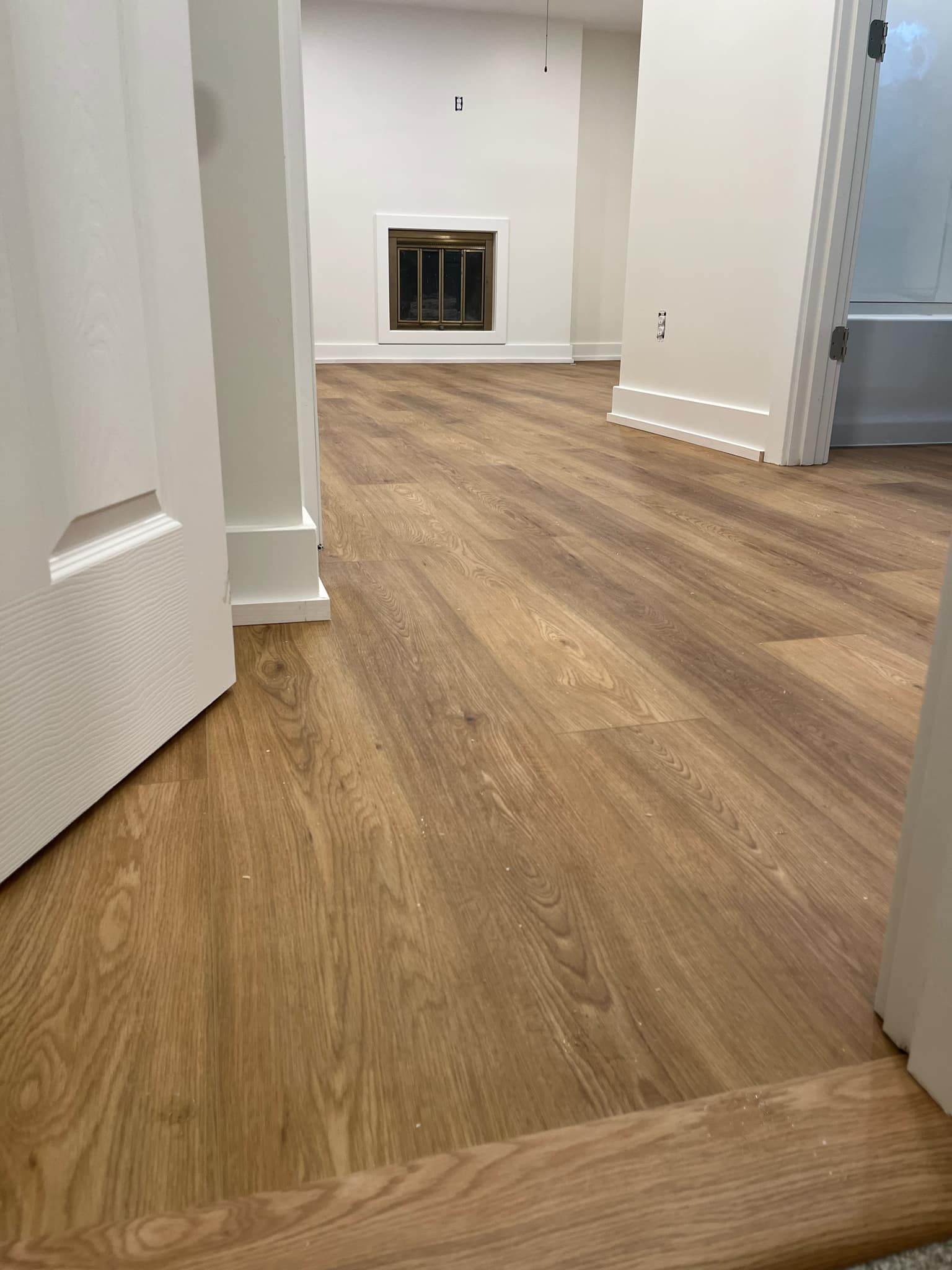A hallway with hardwood floors and a fireplace in a house.