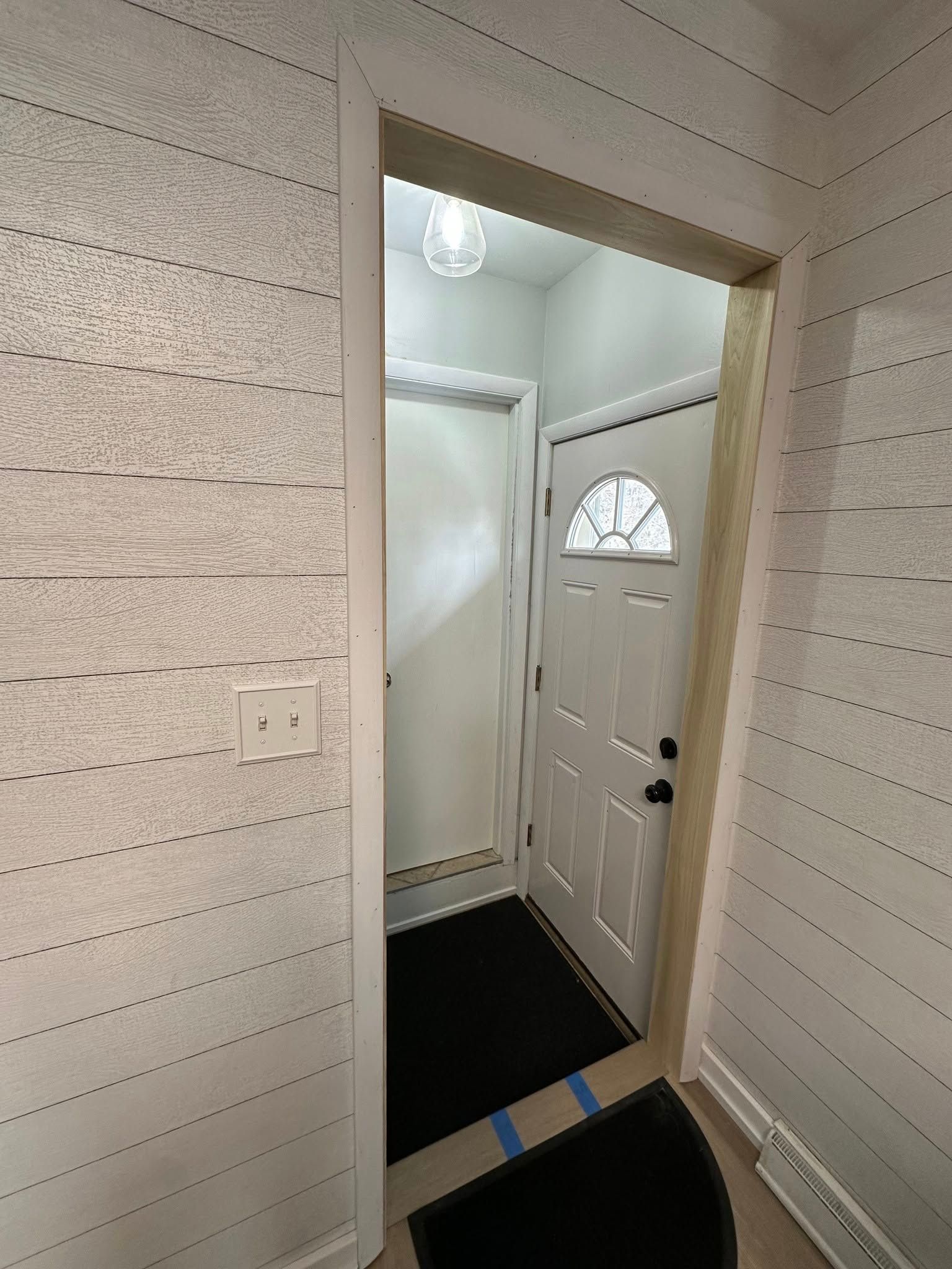 A hallway with a white door and a black mat.