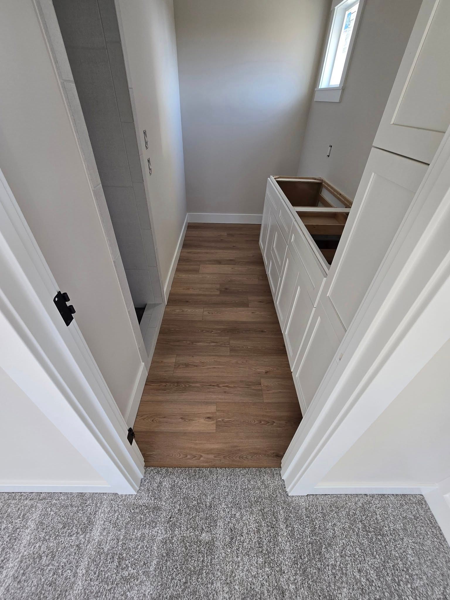 A hallway in a house with wooden floors and white cabinets.