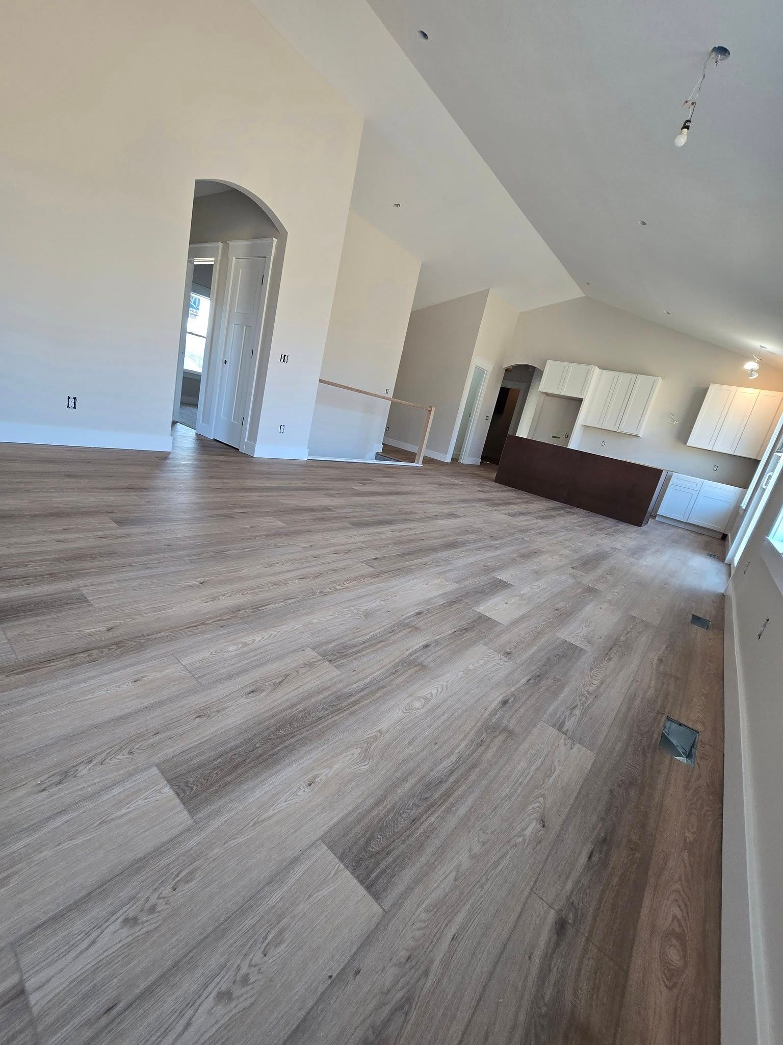 A living room with hardwood floors and a kitchen in the background.