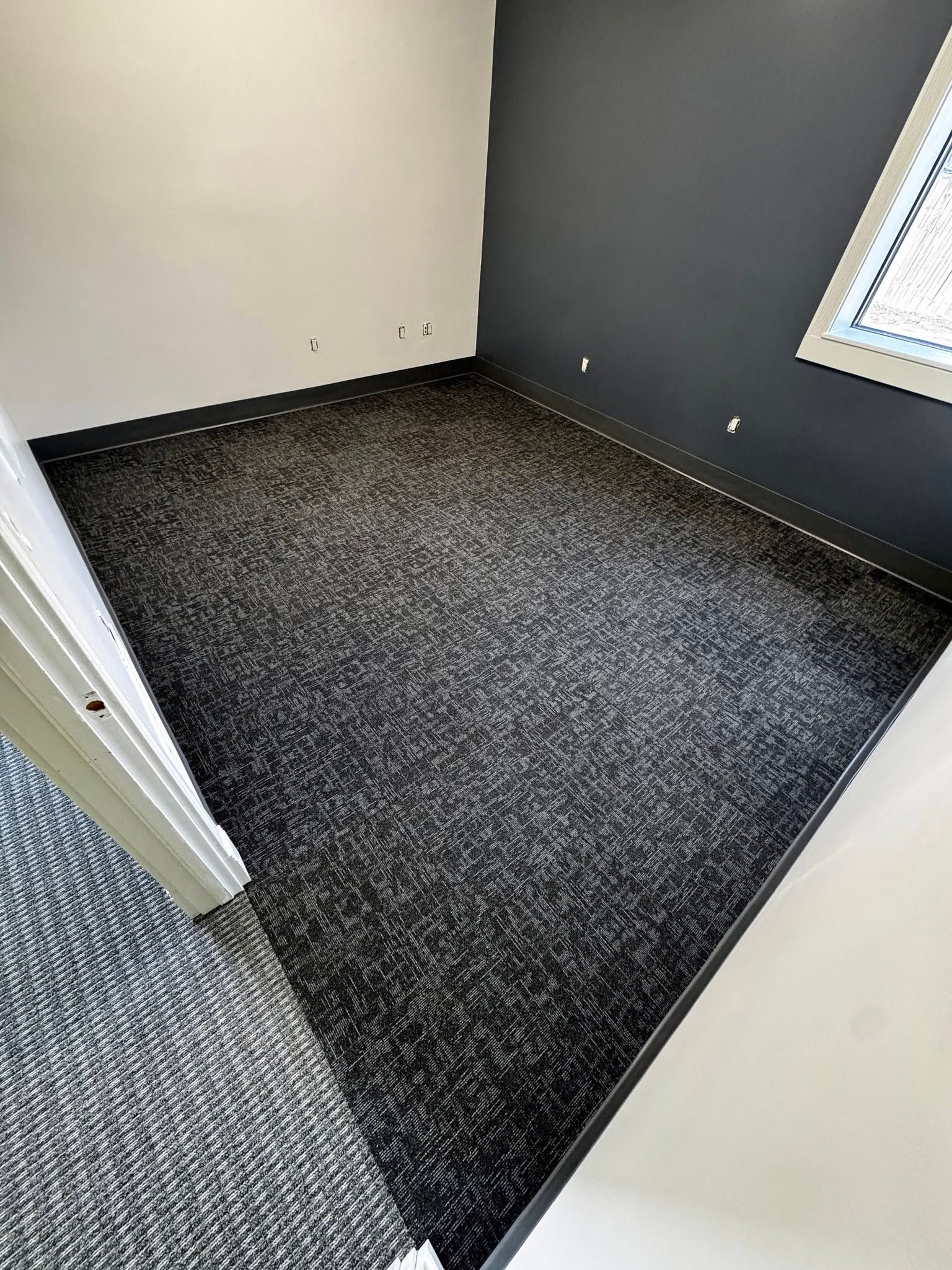 A room with a black carpeted floor and a window.