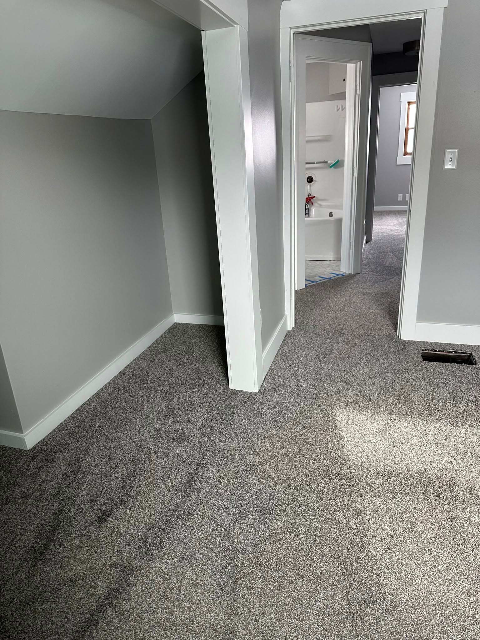 A room with a carpeted floor and a doorway leading to a bathroom.