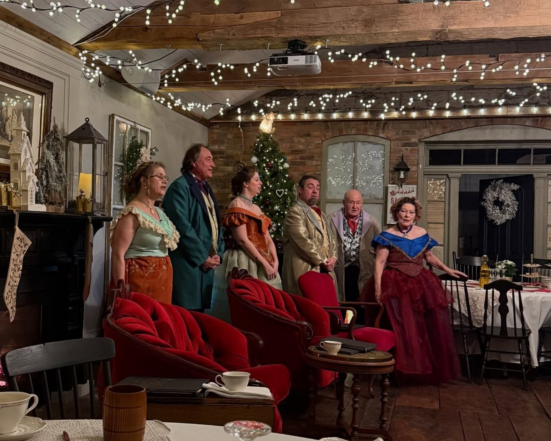 Costumed group standing in a cozy decorated room with string lights and red chairs