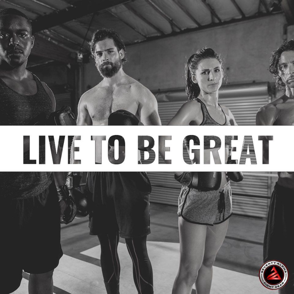 A group of people are standing in a gym with the words `` live to be great '' above them.