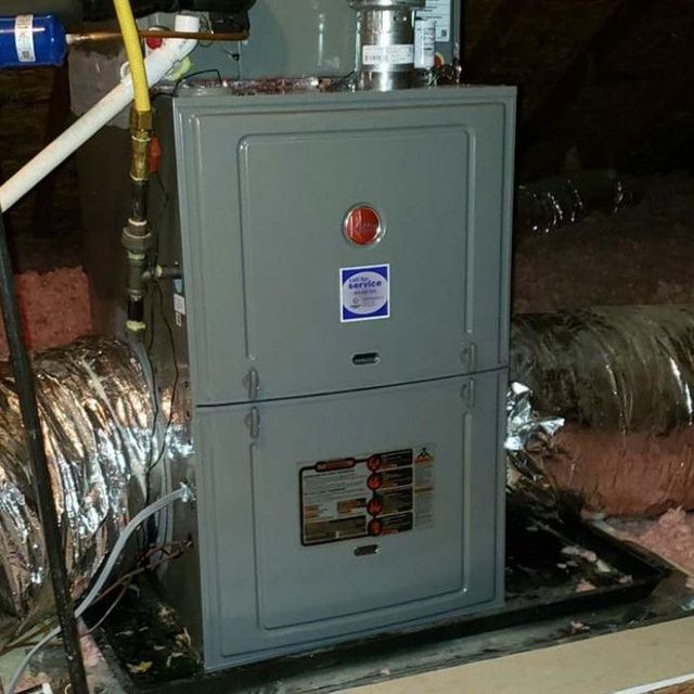 Gray furnace unit in an attic with ductwork and insulation.