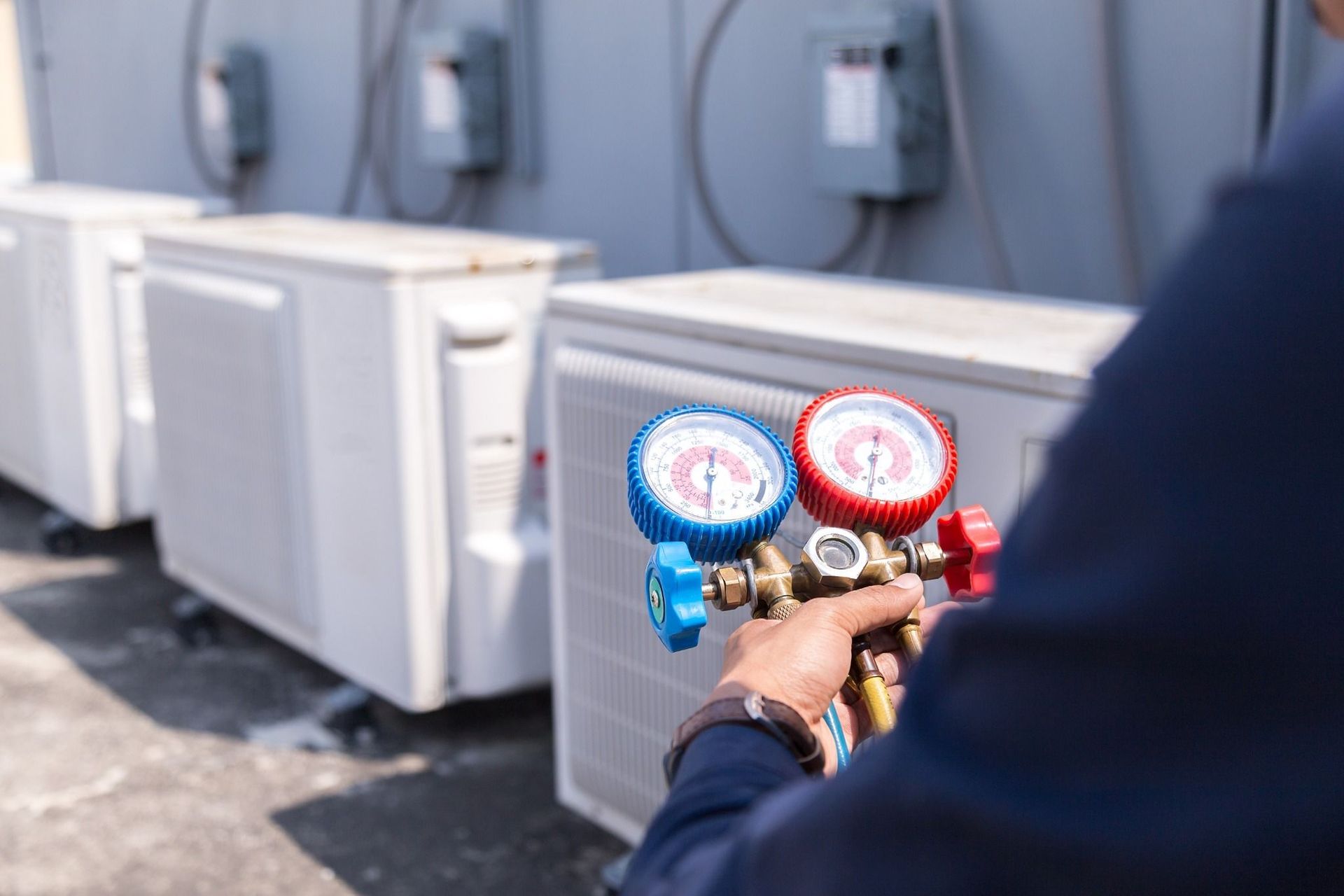HVAC technician checks air conditioning unit's pressure with gauges. Outdoors, sunlight.