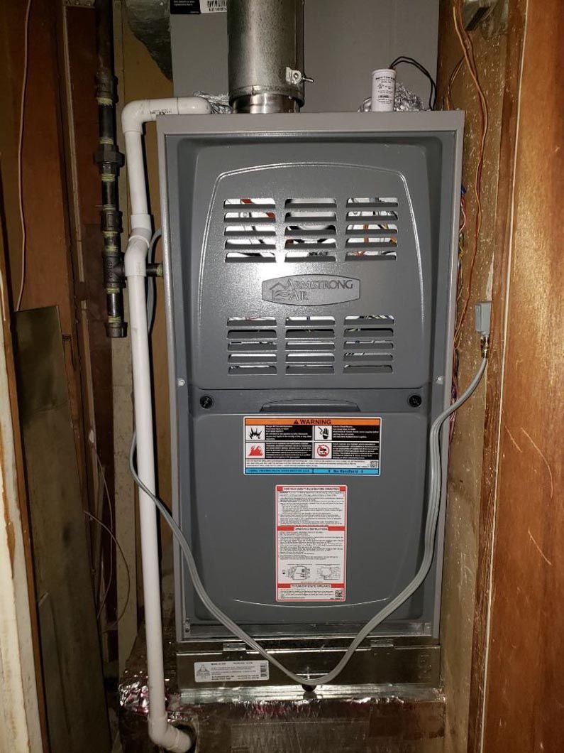 A furnace is sitting in a corner of a room next to a pipe.