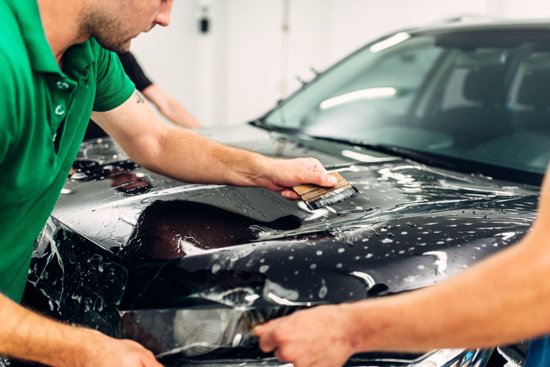 Two people applying film to a black car hood, using squeegees and soapy water.