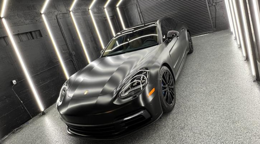Black Porsche Panamera inside a well-lit garage with vertical lights.