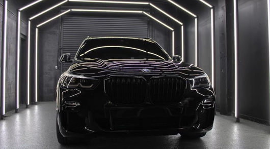 Black BMW SUV inside a garage with white neon lighting.