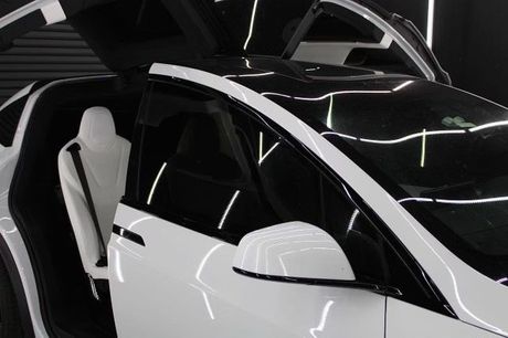 White Tesla with open doors, black glass roof, side mirror visible.