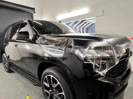 Black SUV with protective film being applied in a garage.