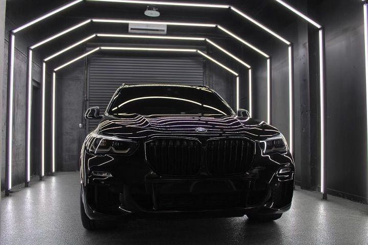 Black BMW SUV in a dark, modern garage, illuminated by white linear lights.