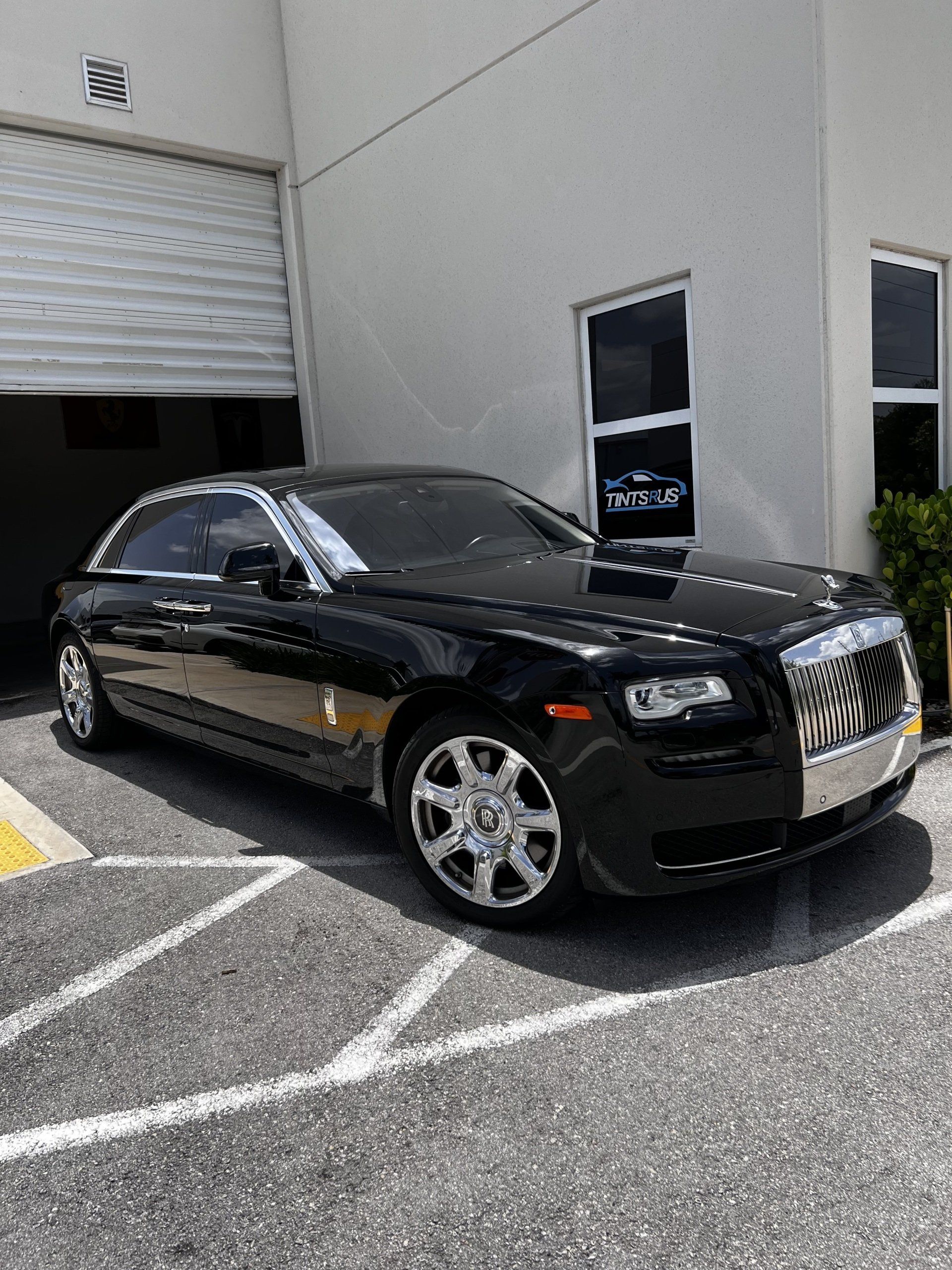Black Rolls-Royce parked in front of a building with an open garage door.