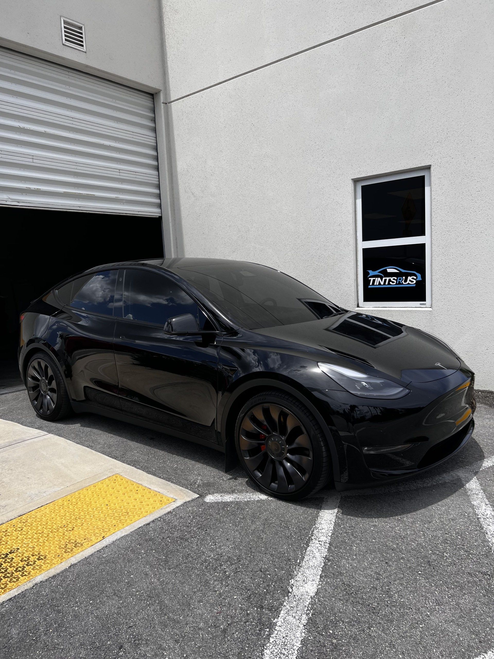 Black Tesla Model Y parked in front of a building with the garage door open.