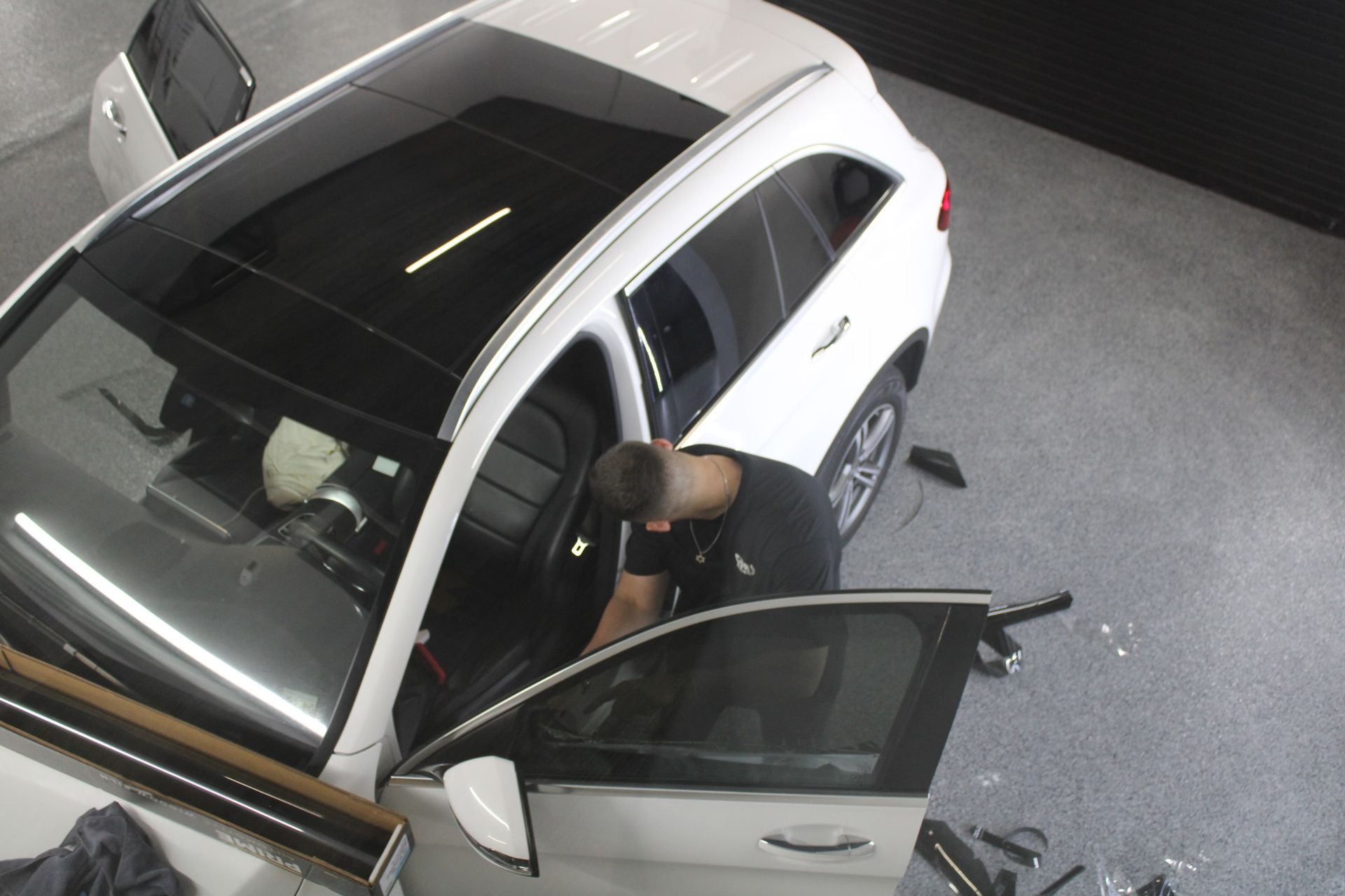 A person tinting a white SUV's windows in a garage; doors open.