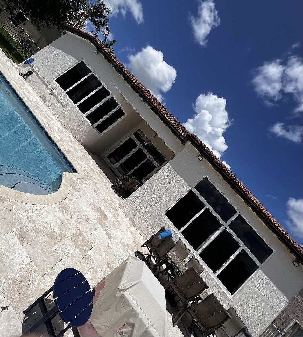 House with pool and outdoor seating against a blue sky with puffy white clouds.